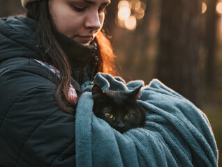 Woman holds a cat in the park. Concept of having fun with a black stray domestic cat in the park and outdoors.