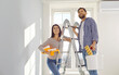 Attractive couple together stand on stepladder with equipment for repair: roller for painting the surface, tray and bucket.