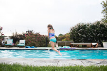 Rear View Of Blonde Girl Jumping Into Backyard Swimming Pool
