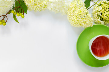 Wall Mural - Сup of hot tea with bouquet of hydrangea on white background.