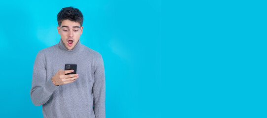 Poster - surprised young man with mobile phone or smartphone isolated on blue background