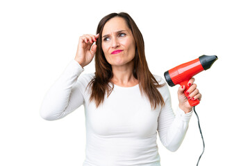 Wall Mural - Middle age woman holding a hairdryer over isolated chroma key background having doubts and with confuse face expression