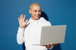 © ViDi Studio - Young happy IT man of African American ethnicity wear white hoody hold use work on laptop pc computer waving hand get video call talk isolated on plain dark royal navy blue background studio portrait