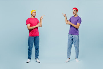 Wall Mural - Full body smiling cheerful cool young couple two friends men wear casual clothes together point index fingers on area between them isolated on pastel plain light blue cyan background studio portrait.