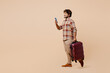 © ViDi Studio - Full body traveler Indian man in casual clothes hold suitcase use mobile cell phone isolated on plain beige background Tourist travel abroad in free time rest getaway Air flight trip journey concept