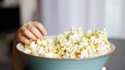 Wall Mural - Little girl is eating popcorn in home kitchen. Focus on hand taking popcorn