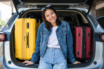 Happy Asian young woman sit on suv car trunk with suitcases