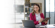 © amnaj - Attractive Asian businesswoman sitting happily using tablet at work and smiling happily.