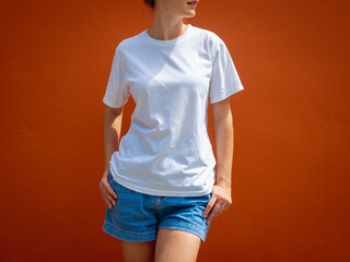 Wall Mural - Female model wearing white blank t-shirt on the background of an orange wall.