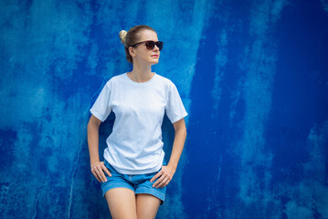 Wall Mural - Female model wearing white blank t-shirt on the background of an blue wall.