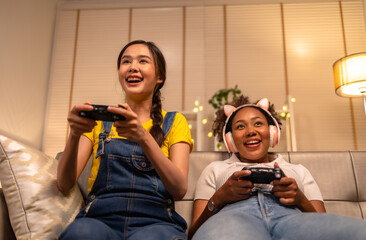 Wall Mural - Young  asian and african woman playing video games at home living room at night.Lesbian couples or lgbt activities on vacation inside the room.