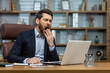 © Liubomir - Mature man yawning inside classic office, senior businessman in workplace sleepless and overworked, boss in business suit sitting at desk, using laptop at work.
