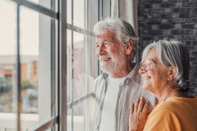 Happy Bonding Loving Middle Aged Senior Retired Couple Standing Near Window, Looking In Distance, Recollecting Good Memories Or Planning Common Future, Enjoying Peaceful Moment Together At Home..