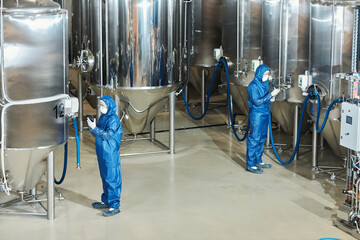 Wide angle view at factory workshop with two workers operating storage tanks