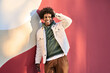 © insta_photos - Young happy African American teen guy laughing on red wall lit with sunlight. Smiling cool ethnic generation z teenager student model standing looking at camera posing for portrait outdoors.