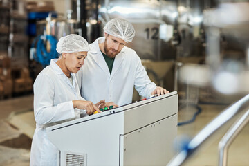 Two workers wearing lab coats operating equipment at food factory