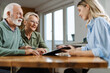 © Goran - Happy senior couple having a meeting with their insurance agent at home