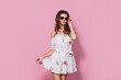 Pretty girl in floral summer dress and sunglasses posing on a pink background. Summer floral outfit