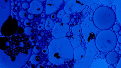 blue abstract background with oil drops and black ink spots floating on a liquid like bacteria