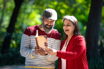 Senior Indian man and woman reading book at park.