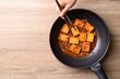 Spicy braised tofu (Dubu Jorim) in cooking pan with hand and chopsticks, Korean side dish, Table top view