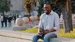 Happy smiling African American ethnic middle-aged man businessman male sitting outdoors in city with coffee tea and phone waiting for date business meeting smile to friend carefree cheerful relaxing