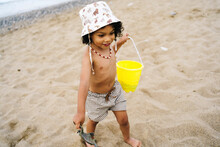 Cute Boy Wearing Hat With Bucket And Toy On Sand At Beach