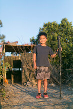 A Little Boy Plays In A Jungle Near A Deserted Soldier Outpost, He Stands Like A Soldier With A Gun Like Stick On His Right Hand.