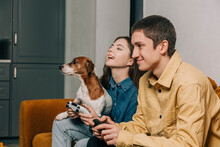 Happy Teenage Couple With Dog Playing Game On Sofa At Home