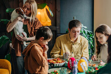 Happy Woman Holding Dog With Family Having Easter Dinner At Home