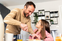 Happy father serving breakfast to daughter at table