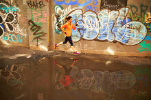 Woman Running Past Puddle In Graffiti Lined Alleyway In Boston, Massachusetts, USA