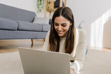 Happy Young Woman Using Laptop Lying On Carpet At Home