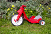 A Child’s Red Big Wheel Toy On The Grass