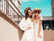 © halayalex - Two young beautiful smiling hipster female in trendy summer white dress clothes and straw hats. Sexy carefree women walking in street. Positive models having fun, hugging and laughing