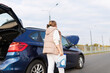 © Ivan Traimak - a woman with a canister of liquid for engine cooling near a broken down car with a raised trunk and hood