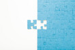 © fotoduets - Unfinished blue puzzle with last one piece on white table background. Closeup. Top down view.