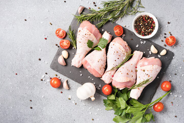 Wall Mural - Raw chicken drumsticks with seasonings and vegetables on black slate plate over light gray concrete background. Chicken legs ready to cook. Organic meat, healthy eating concept