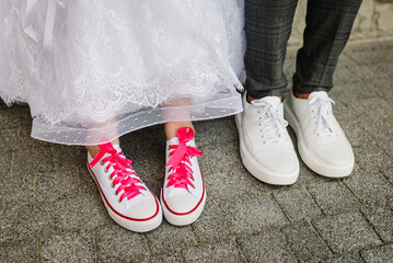 The bride and groom wearing pink sneakers. Concept funny wedding couple. The newlywed together. Textile sneakers flat shoes. Close up. Top view. View of the bottom of the feet and shoes.