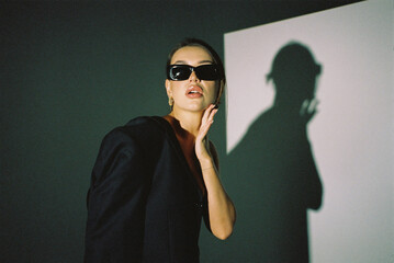 Wall Mural - A modern fashion photo taken with a film camera. A female model in sunglasses poses in the studio on a white background