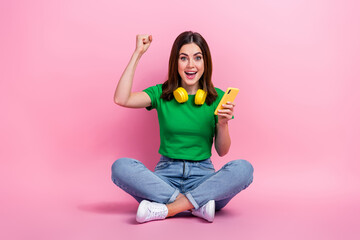 Sticker - Full size portrait of delighted funky girl sit floor hold smart phone raise fist success isolated on pink color background