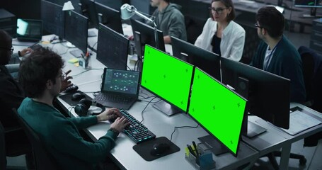 Team of Young Professionals Working in a Technological Research and Development Agency. Software Programmer Working on a Computer with Two Green Screen Mock Up Displays. Elevated High Angle Footage