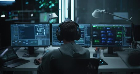 Wall Mural - Lone Hacker Breaks Into Government Data Servers and Infects Their System with an Exploit Software. His Hideout Place is in Dark Technological Facility with Multiple Displays. Footage from the Back