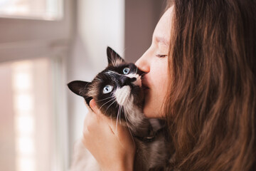 Wall Mural - Close up of lovely young woman kissing cat at home