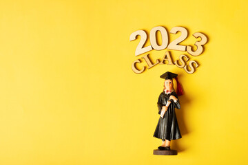 Class of 2023 concept. Wooden number 2023 with graduate statuette on color background