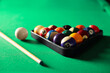 Plastic triangle rack with billiard balls and cue on green table, closeup