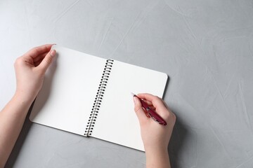 Canvas Print - Woman writing in notebook with pen at light grey table, top view. Space for text