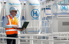 Man Works For Energy Company. Engineer Stands Among Hydrogen Equipment. Mechanic With Laptop Controls Process Of Obtaining Energy. Man Inspects Hydrogen Power Plant. Getting Electricity  Hydrogen H2