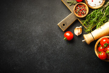 Wall Mural - Ingredients for cooking on black stone kitchen table. Herbs, spices and vegetables with wooden cutting board. Flat lay.