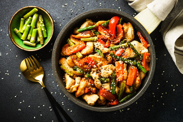 Poster - Chicken stir fry with vegetables in the skillet at black stone background. Top view with copy space.